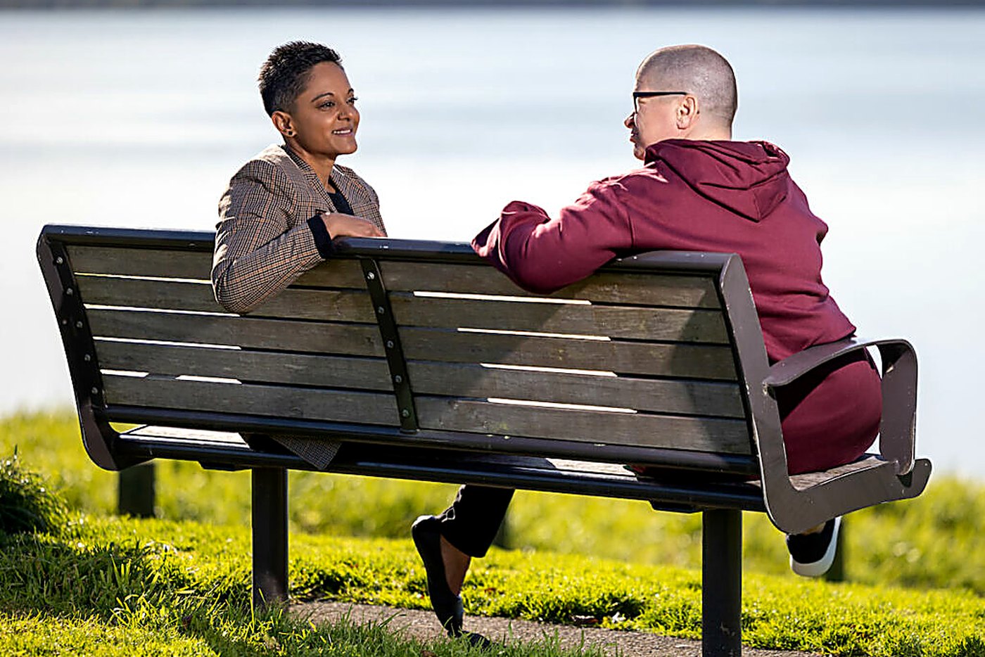 Two people talking on a park bench overlooking water